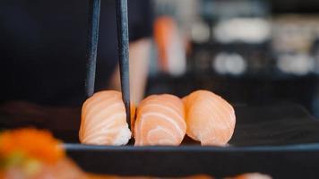 donna asiatica che mangia sushi in un ristorante giapponese, giovane donna che tiene le bacchette e mangia sushi di salmone all'ora di pranzo in estate. donne di stile di vita che mangiano il concetto di cibo tradizionale. foto