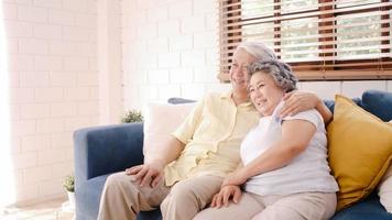coppia di anziani asiatici che guardano la televisione nel soggiorno di casa, una dolce coppia si gode il momento dell'amore mentre è sdraiata sul divano quando è rilassata a casa. godendo il concetto di famiglia senior di stile di vita del tempo a casa. foto