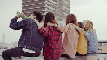 gruppo di giovani donne asiatiche e uomini persone che ballano e alzano le braccia in aria per la musica suonata da dj al tramonto festa urbana sul tetto. giovani ragazze asiatiche e ragazzi che vanno in giro con le bevande foto