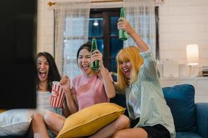 gruppo di donne asiatiche festa a casa, femmina che beve birra guardando la tv tifare calcio momento divertente insieme sul divano nel soggiorno di notte. adolescente giovane amico tifoso di calcio, celebra il concetto di vacanza. foto