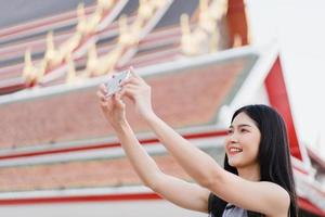 la donna asiatica del viaggiatore che usa il telefono cellulare per scattare una foto mentre trascorre un viaggio di vacanza a bangkok, in tailandia, la femmina si gode il viaggio in uno straordinario punto di riferimento in città. stile di vita le donne viaggiano nel concetto di città.