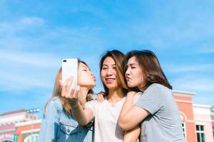 belle donne asiatiche attraenti degli amici che utilizzano uno smartphone. felice giovane adolescente asiatica in città urbana mentre scatta autoritratti con i suoi amici insieme a uno smartphone. foto