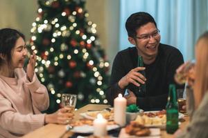 buon natale e felice anno nuovo gruppo di giovani amici a cena a casa. festa di famiglia asiatica con birra e pizza vicino all'albero di natale a casa di notte. festa di celebrazione e stare insieme. foto