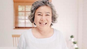 donna anziana asiatica che si sente felice sorridendo e guardando alla telecamera mentre si rilassa sul divano nel soggiorno di casa. stile di vita donne anziane a casa concetto. foto