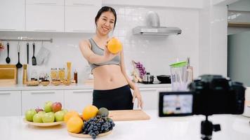 blogger sportiva donna asiatica utilizzando la videocamera che registra come fare il video del succo d'arancia per il suo abbonato, le donne usano frutta biologica che fa il succo d'arancia da sola a casa. concetto di cibo sano. foto