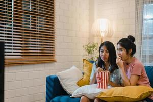 le donne lesbiche lgbt si accoppiano guardando film a casa, amante asiatica che mangia popcorn spaventoso e shock mentre guarda un film horror insieme sul divano nel soggiorno nel concetto di notte. foto