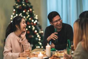 buon natale e felice anno nuovo gruppo di giovani amici a cena a casa. festa di famiglia asiatica con birra e pizza vicino all'albero di natale a casa di notte. festa di celebrazione e stare insieme. foto