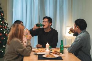 buon natale e felice anno nuovo gruppo di giovani amici a cena a casa. festa di famiglia asiatica con birra e pizza vicino all'albero di natale a casa di notte. festa di celebrazione e stare insieme. foto