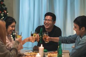 buon natale e felice anno nuovo gruppo di giovani amici a cena a casa. festa di famiglia asiatica con birra e pizza vicino all'albero di natale a casa di notte. festa di celebrazione e stare insieme. foto