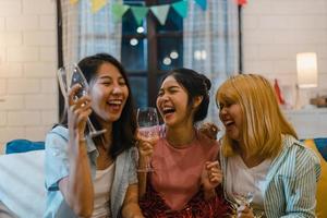 gruppo di donne asiatiche festa a casa, cocktail femminile che parla divertendosi insieme sul divano nel soggiorno di notte. adolescente giovane amico gioca, amicizia, celebra il concetto di vacanza. foto