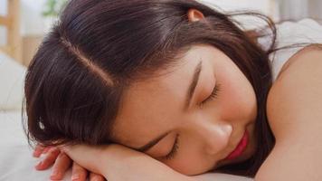 donna asiatica che sogna mentre dorme sul letto in camera da letto, bella femmina giapponese che usa il tempo di relax sdraiato sul letto a casa. le donne di stile di vita che usano il tempo di relax a casa concetto. foto