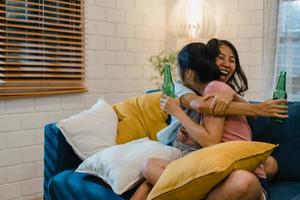 donne lesbiche lgbt coppia festa a casa, donna asiatica che beve birra guardando la tv tifo calcio momento divertente insieme sul divano nel soggiorno di notte. giovane tifoso amante del calcio, celebra il concetto di vacanza. foto