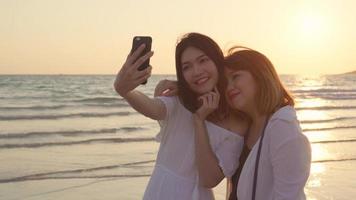 giovane coppia lesbica asiatica utilizzando smartphone prendendo selfie vicino alla spiaggia. belle donne lgbt coppia felice relax goditi il momento dell'amore quando il tramonto in serata. stile di vita coppia lesbica viaggio sul concetto di spiaggia foto