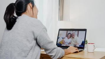 giovane donna asiatica d'affari che utilizza la videochiamata del laptop parlando con il papà e la mamma di famiglia mentre lavora da casa nella camera da letto. autoisolamento, distanziamento sociale, quarantena per la prevenzione del virus corona. foto