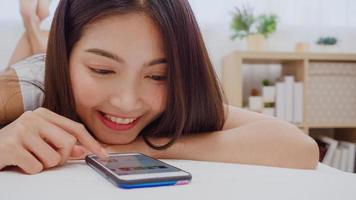 giovane donna asiatica che usa lo smartphone controllando i social media sentendosi felice sorridente mentre si trova sul letto dopo essersi svegliata al mattino, bella ragazza giapponese attraente sorridente si rilassa in camera da letto a casa. foto