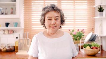 donna anziana asiatica che si sente felice sorridendo e guardando alla telecamera mentre si rilassa in cucina a casa. stile di vita donne anziane a casa concetto. foto
