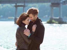 bella incredibile divertente allegra giovane coppia che si abbraccia all'aperto vicino al fiume sullo sfondo del ponte. fidanzata e fidanzato. concetto di famiglia, amore e amicizia foto