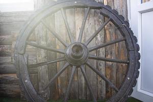 dimenticata vecchia ruota di carro in legno appoggiata a una parete di legno. ruote di carro al vecchio muro di legno della casa. foto