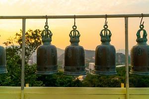 campane metalliche appese in fila fuori nel tempio buddista tailandese foto