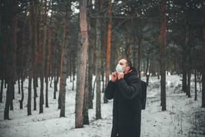 giovane con i capelli corti in una maschera medica nella foresta invernale. foto