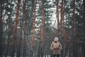 attraente ragazza bionda e una tazza di bevanda calda passeggiate nella foresta d'inverno. foto