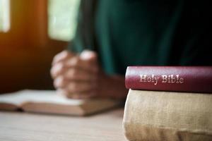 uomo con la Bibbia che prega, le mani giunte insieme sulla sua Bibbia sul tavolo di legno. foto