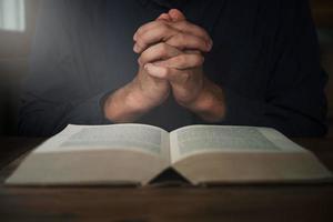 l'uomo sta leggendo e pregando la Scrittura o la Sacra Bibbia su un tavolo di legno con spazio per la copia. religione, credo concetto. foto
