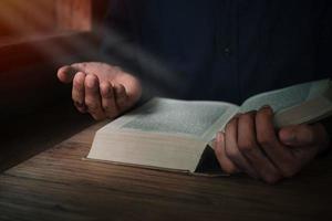 l'uomo sta leggendo e pregando la Scrittura o la Sacra Bibbia su un tavolo di legno con spazio per la copia. religione, credo concetto. foto