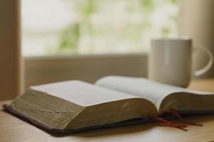 primo piano della Bibbia aperta con una tazza di caffè per la devozione mattutina su un tavolo di legno con luce della finestra. sfondo cristiano foto