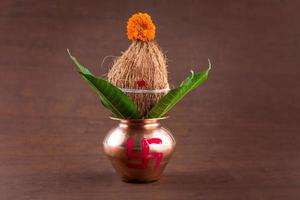 kalash in rame con cocco e foglia di mango con decoro floreale su fondo di legno. essenziale nella puja indù. foto