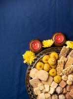 dolci indiani tradizionali su sfondo blu con candele e fiori piatti foto