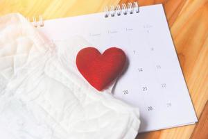 assorbente igienico o assorbente femminile sul calendario con cuore rosso - igiene femminile significa fogli assorbenti del prodotto mestruale per le donne foto