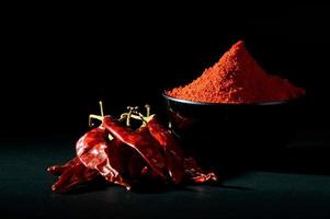 polvere fredda in una ciotola nera con peperoncino rosso, peperoncino secco su sfondo nero foto