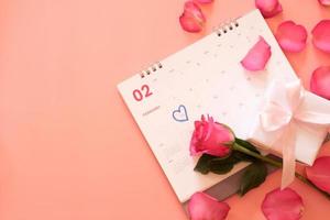rosa rosa e una confezione regalo sul calendario con petali di rosa isolati su sfondo rosa con copyspace per il testo. concetto di san valentino. pianificazione pianificazione agenda, evento, organizzatore San Valentino. foto