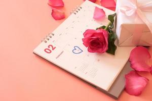 rosa rosa e una confezione regalo sul calendario con petali di rosa isolati su sfondo rosa con copyspace per il testo. concetto di san valentino. pianificazione pianificazione agenda, evento, organizzatore San Valentino. foto