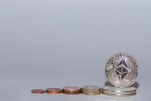 monete in euro e monete etere di valore da criptovaluta impilate in una riga con il grigio foto