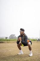 giovane uomo sportivo indiano che fa squat nel campo. concetto di sport e stile di vita sano. foto