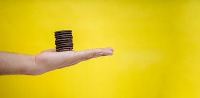 mani che tengono i biscotti al cioccolato su uno sfondo giallo con spazio per la copia foto