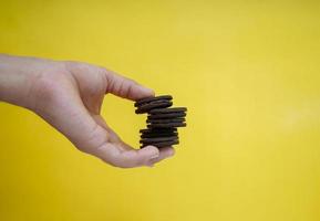 mani che tengono i biscotti al cioccolato su uno sfondo giallo con spazio per la copia foto