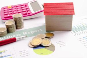 casa rossa e pila di monete con penna e calcolatrice sul rapporto di finanza aziendale foto