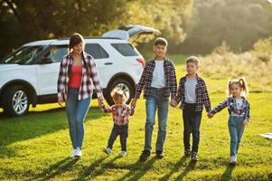 famiglia che trascorre del tempo insieme. madre con quattro bambini in piedi e tenendosi per mano contro un'auto suv bianca. foto