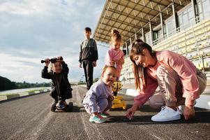 giovane madre alla moda con quattro bambini all'aperto. la famiglia sportiva trascorre il tempo libero all'aria aperta con scooter e pattini. foto