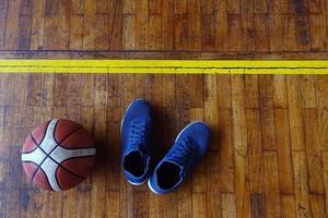 vista dall'alto di scarpe e pallacanestro sul campo da basket in legno foto