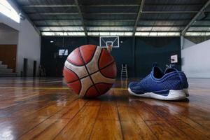 primo piano di scarpe e palla da basket sul campo di legno con canestro da basket sullo sfondo foto