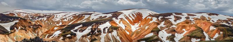 panoramico incredibile paesaggio islandese di colorate montagne vulcaniche arcobaleno landmannalaugar, al famoso sentiero escursionistico laugavegur con drammatico cielo innevato e suolo vulcanico rosso in islanda foto