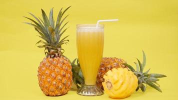 frutta di ananas e un bicchiere di succo isolato su uno sfondo giallo foto