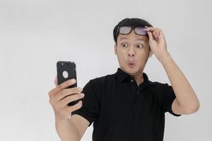 wow il viso del tuo uomo asiatico ha scioccato ciò che vede nello smartphone su sfondo grigio isolato. indonesia uomo indossare camicia nera isolato sfondo grigio foto