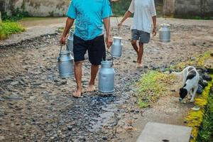 il tradizionale lavoratore lattiero-caseario o l'uomo del latte a Boyolali, in Indonesia, portano un contenitore per il latte lucido in metallo o un bollitore tradizionale dalla fattoria tradizionale foto