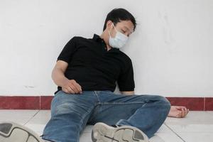 l'influenza dell'uomo asiatico malato è seduto a terra a casa con l'uso della maschera. malattia, influenza, concetto di dolore. concetti di assistenza sanitaria e corona. messa a fuoco selettiva foto