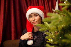 ritratto di una donna carina con un cappello di Babbo Natale vicino all'albero di natale foto